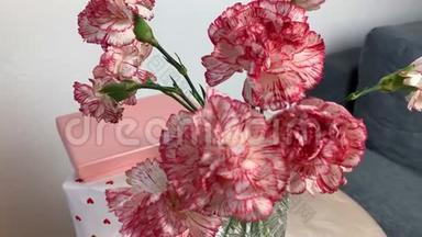 一束粉红色的康乃馨花放在花瓶里，盒子里的礼物放在一张灰色沙发旁边的圆桌上，甜蜜的概念